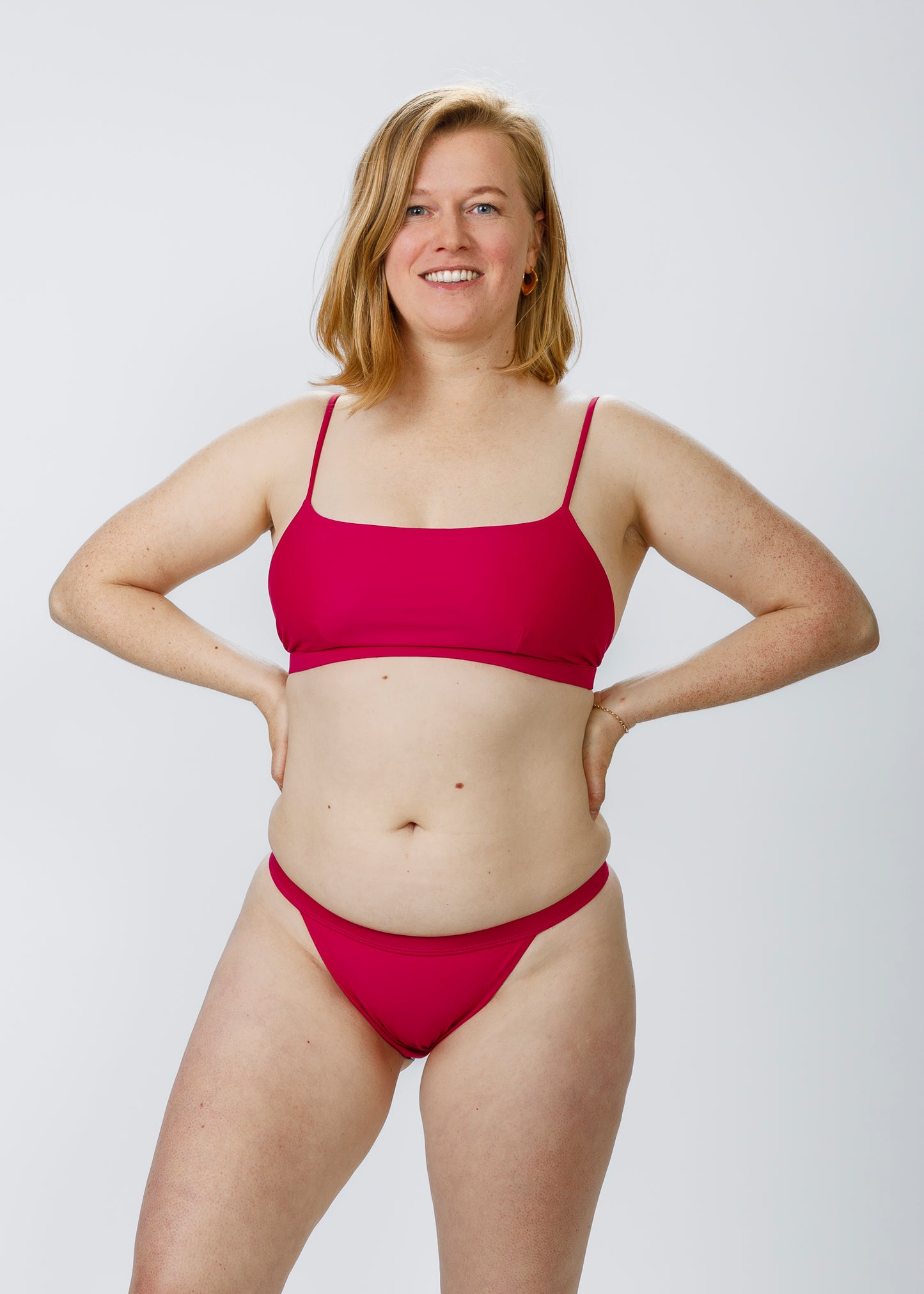 A woman standing with hands on hips, showcasing the flattering fit of Tamara’s classic low-rise pink bikini bottoms, crafted sustainably for active beachwear.