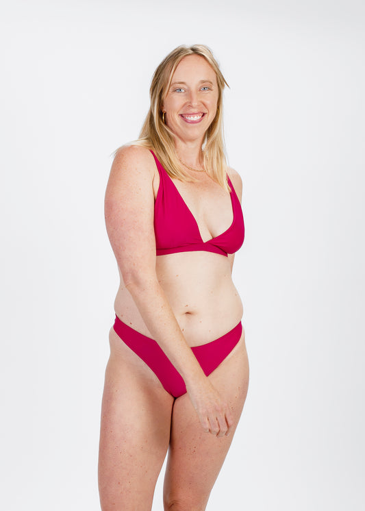 Model smiling in a magenta bikini, looking at the camera with a joyful expression, captured in a bright studio environment.