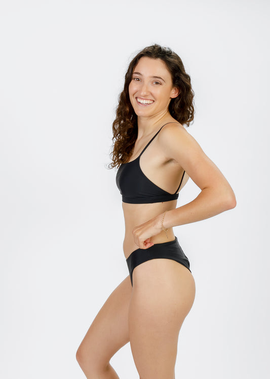 Side view of woman smiling and modelling Tamara’s sustainably designed black square-neck bikini top, highlighting its flattering shape and comfort.