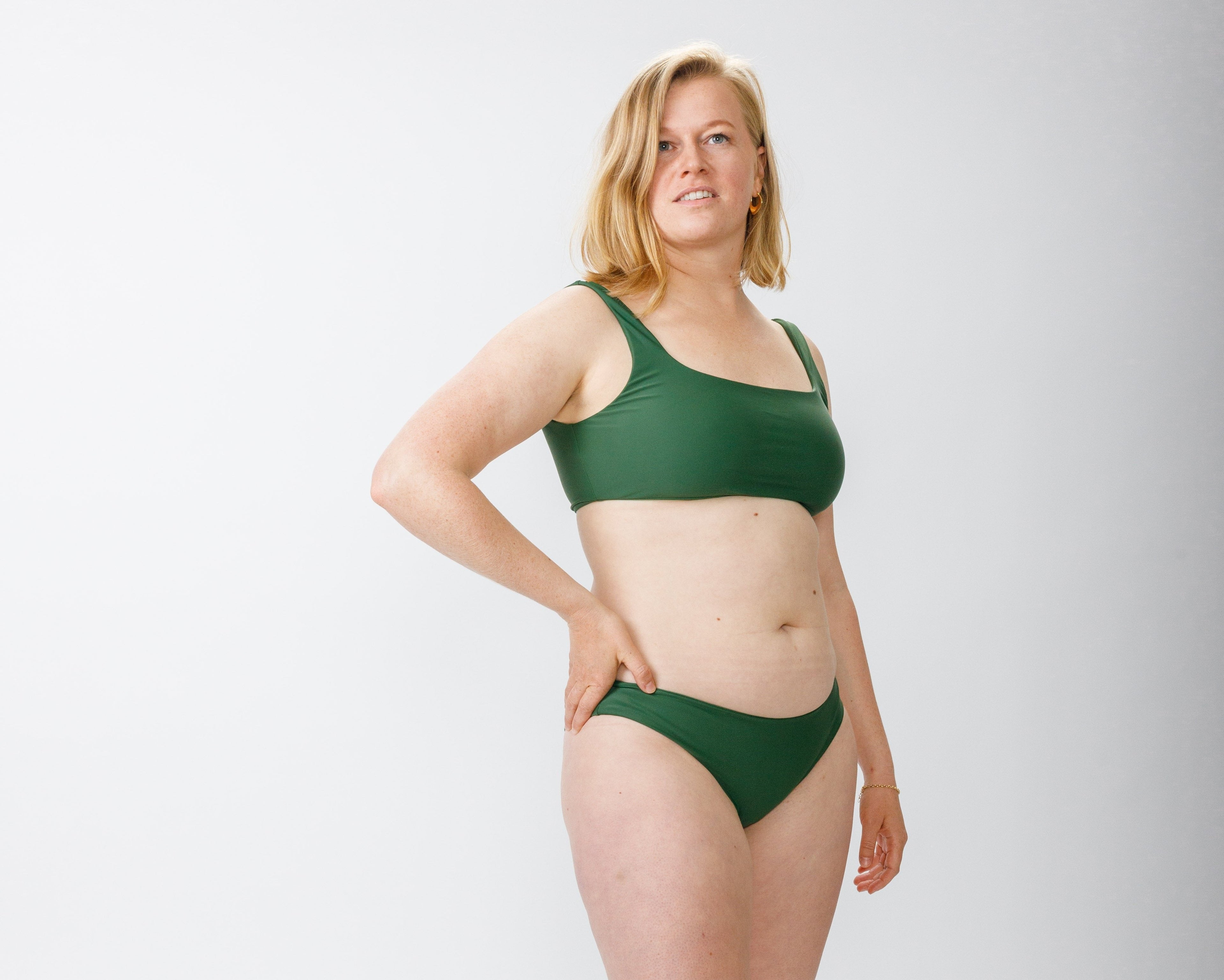 A model wearing a forest green bikini standing confidently against a white background, showcasing the simple and comfortable design of the swimwear.