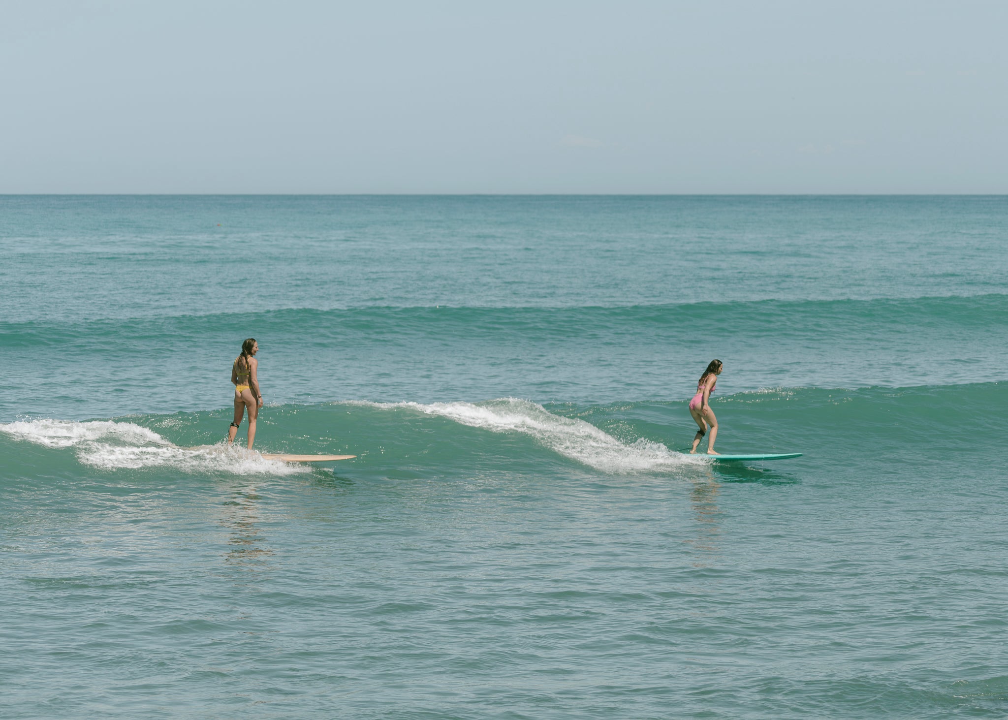 Two women surfing on gentle waves, showcasing Tamara™ swimwear designed for active water sports.