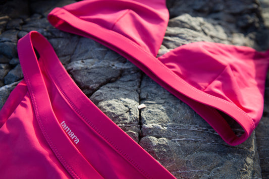 Close-up image of a sustainable pink bikini set by Tamara lying elegantly on textured coastal rocks, highlighting the sleek design and quality fabric.