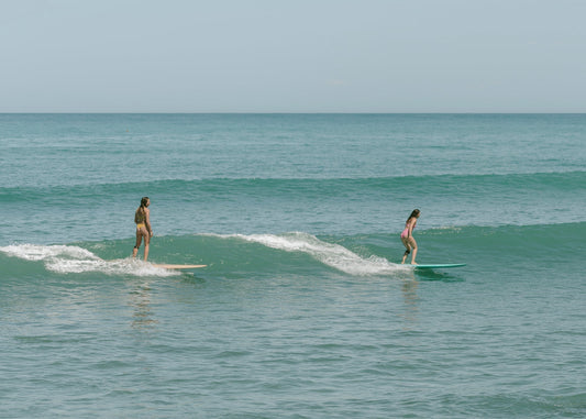 Two women confidently surfing gentle waves, showcasing Tamara's sustainable swimwear designed for active, adventurous women.