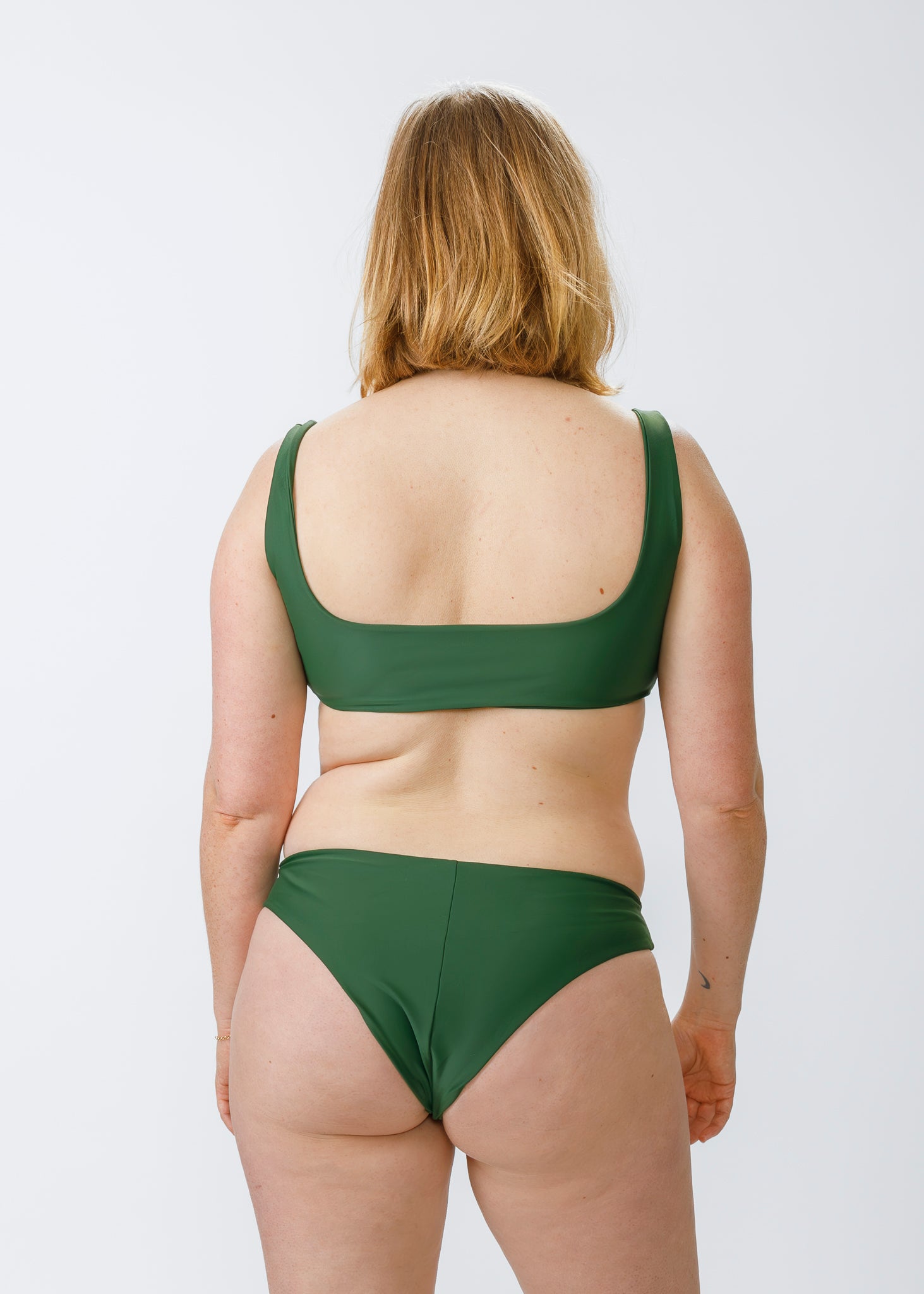 Woman with blonde hair wearing a green, square-neck bikini top and matching bottoms, shown from behind against a white background.