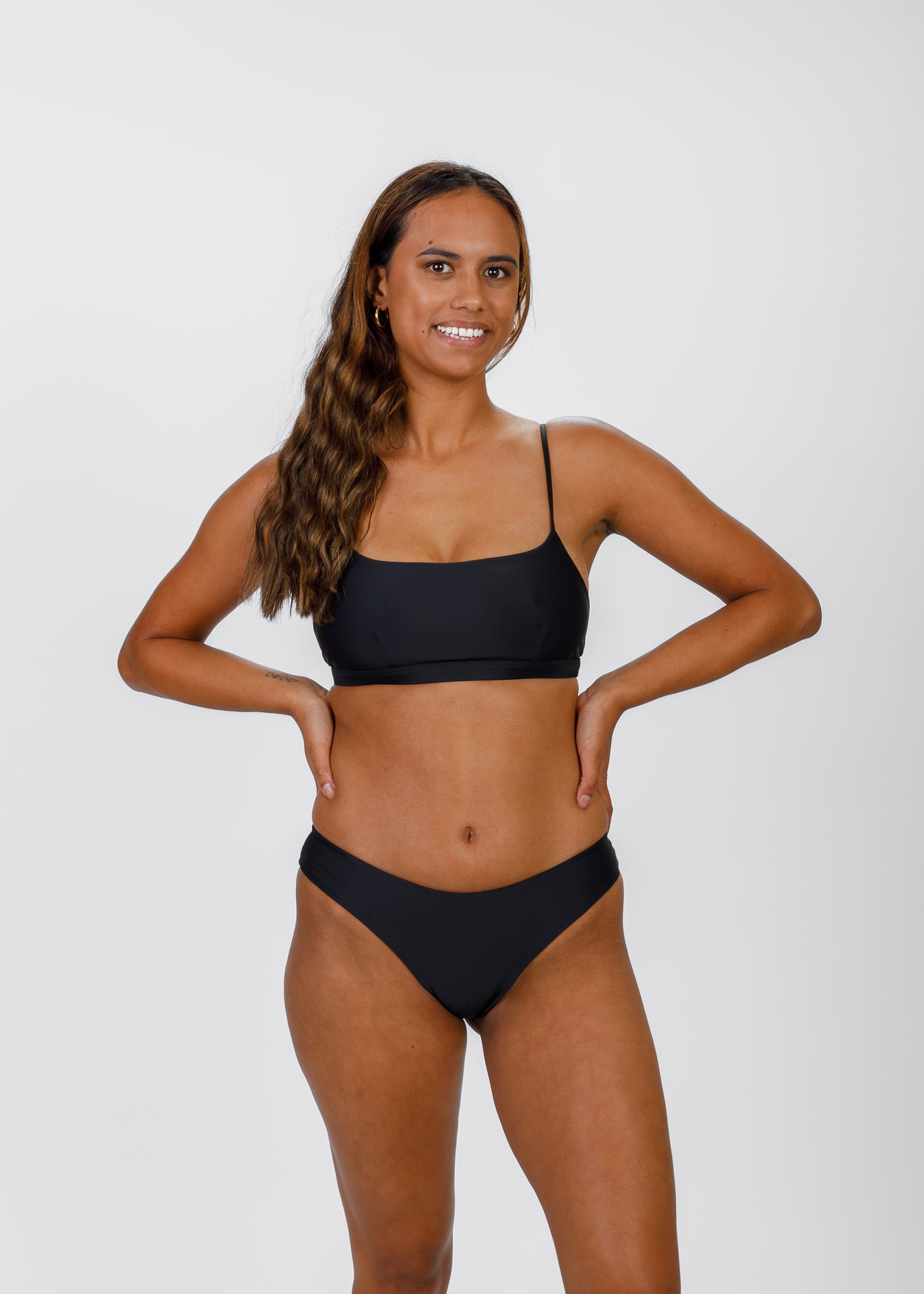 Woman posing confidently in Tamara’s classic black square-neck bikini top, perfect for stylish beach days and active water adventures.