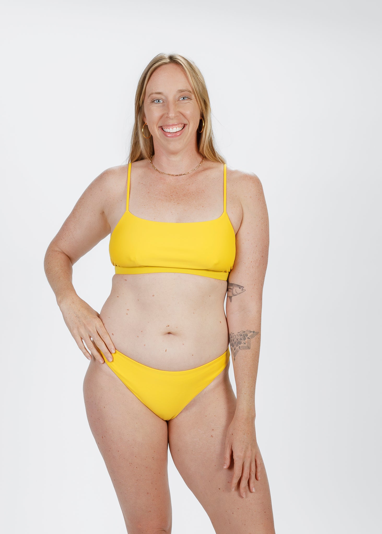 Smiling woman wearing a bright yellow square-neck bikini top by Tamara, designed with thin straps and sustainable materials for comfortable beachwear.