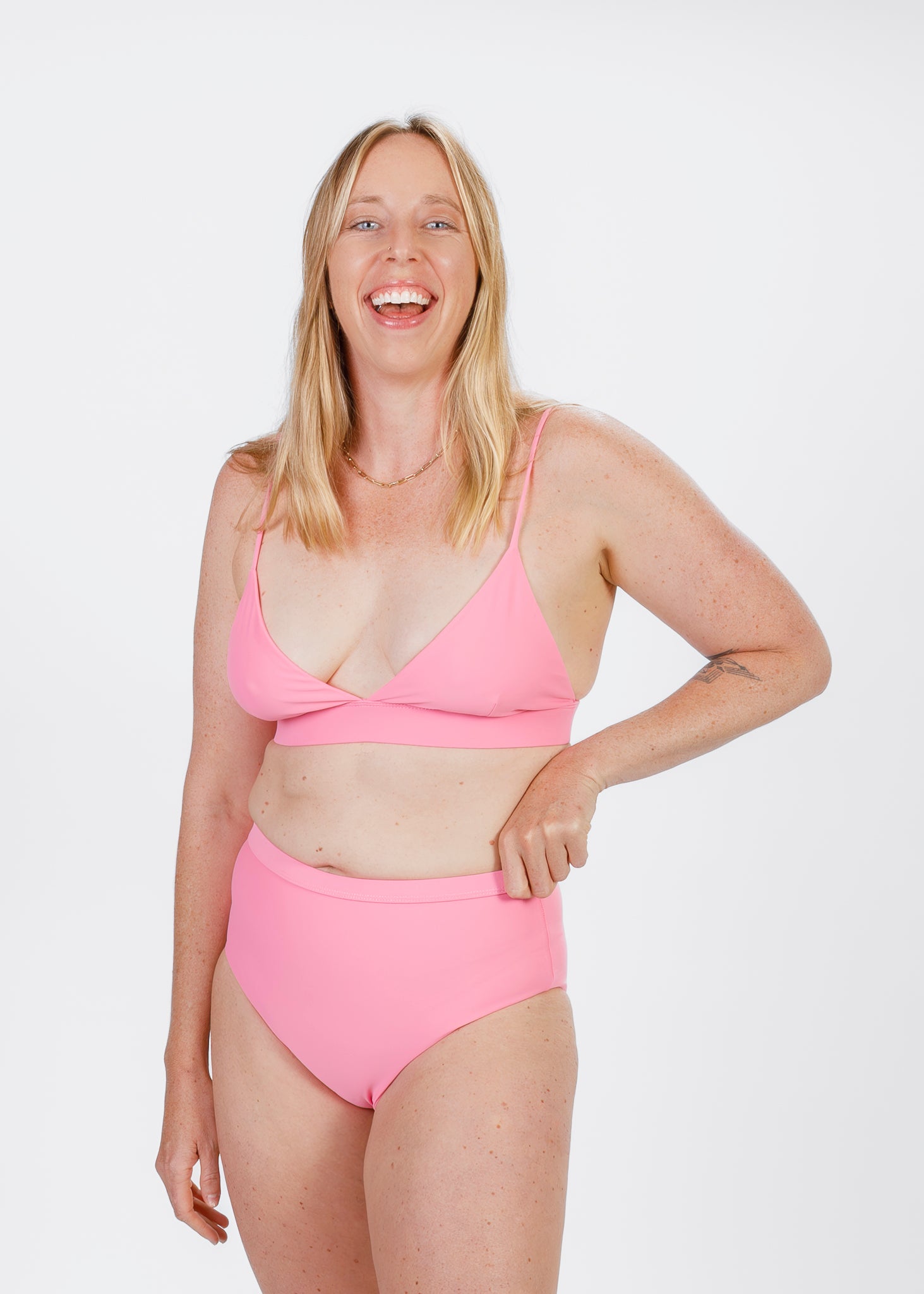 The same blonde woman bursts into laughter while wearing a pink triangle bikini top with a secure underband. Her high-waisted bottoms complete the look, reflecting a fun, carefree approach to swimwear.