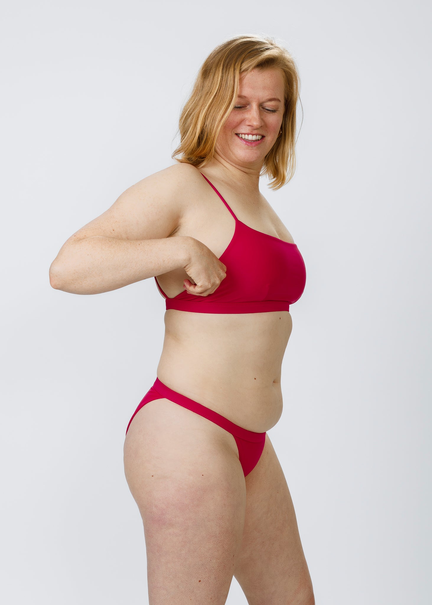Side angle of a woman comfortably adjusting the fit of her pink square-neck bikini top by Tamara, highlighting the sleek and supportive cut.