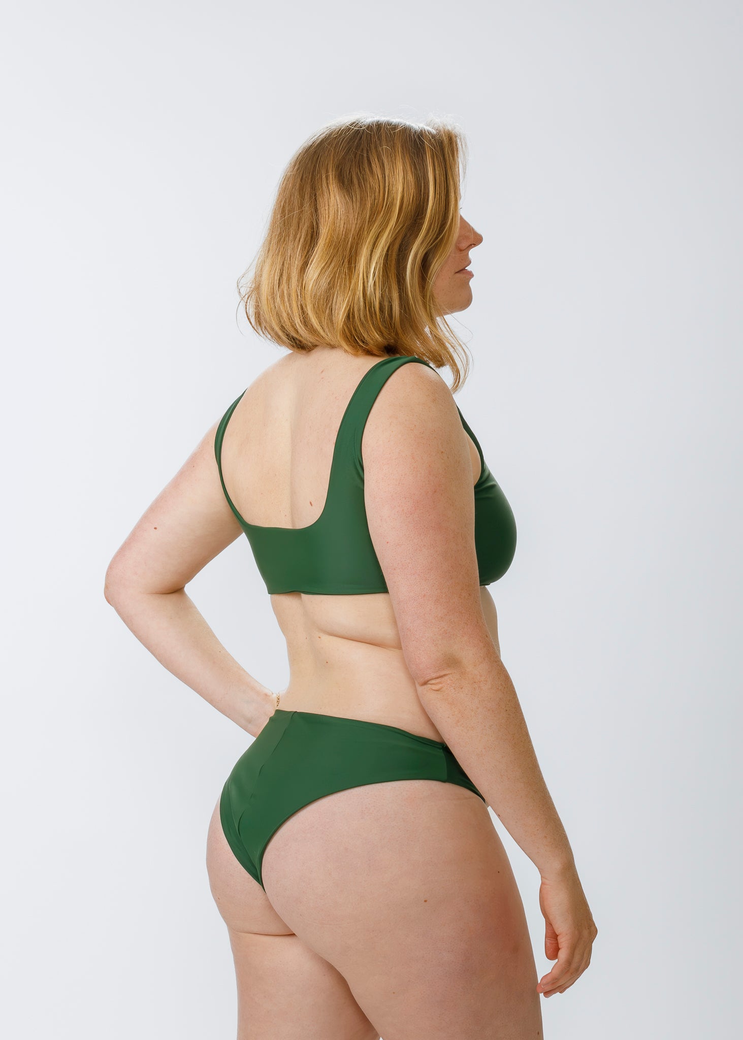 Woman with blonde hair shown from the side, wearing a green square-neck bikini top, highlighting the back scoop and wide shoulder straps.