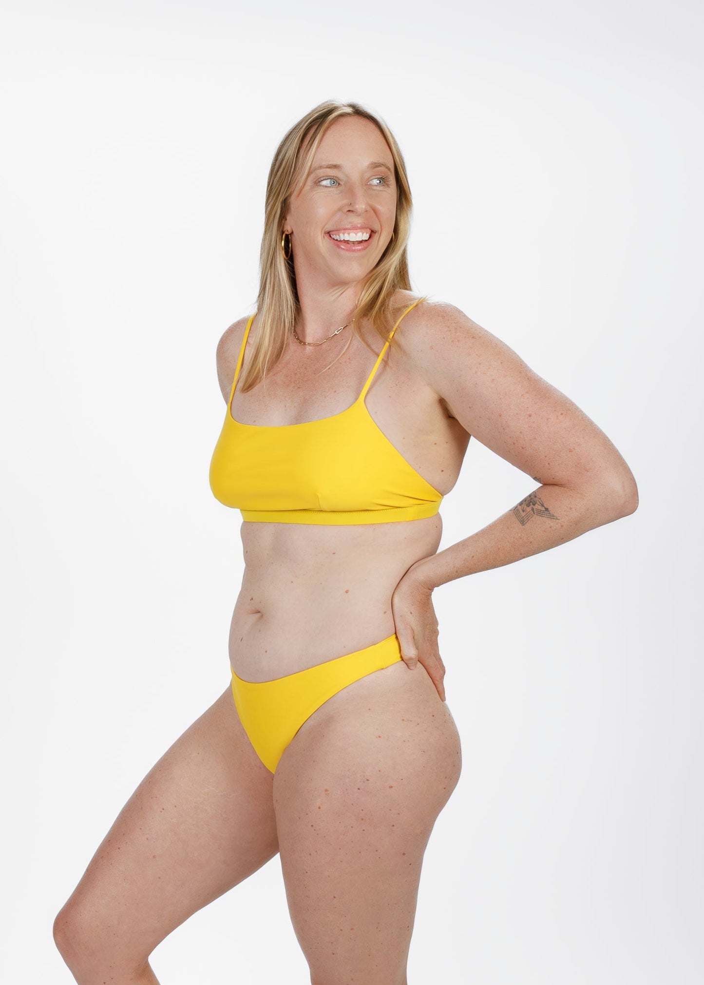 Side angle of a smiling woman in a vibrant yellow square-neck bikini top from Tamara, highlighting the supportive fit and minimalist design.