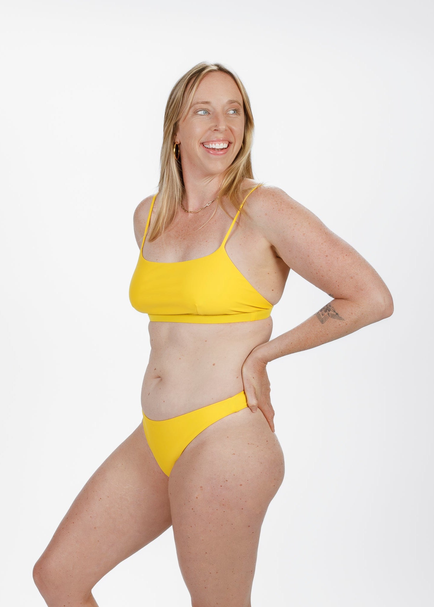 Side angle of a smiling woman in a vibrant yellow square-neck bikini top from Tamara, highlighting the supportive fit and minimalist design.