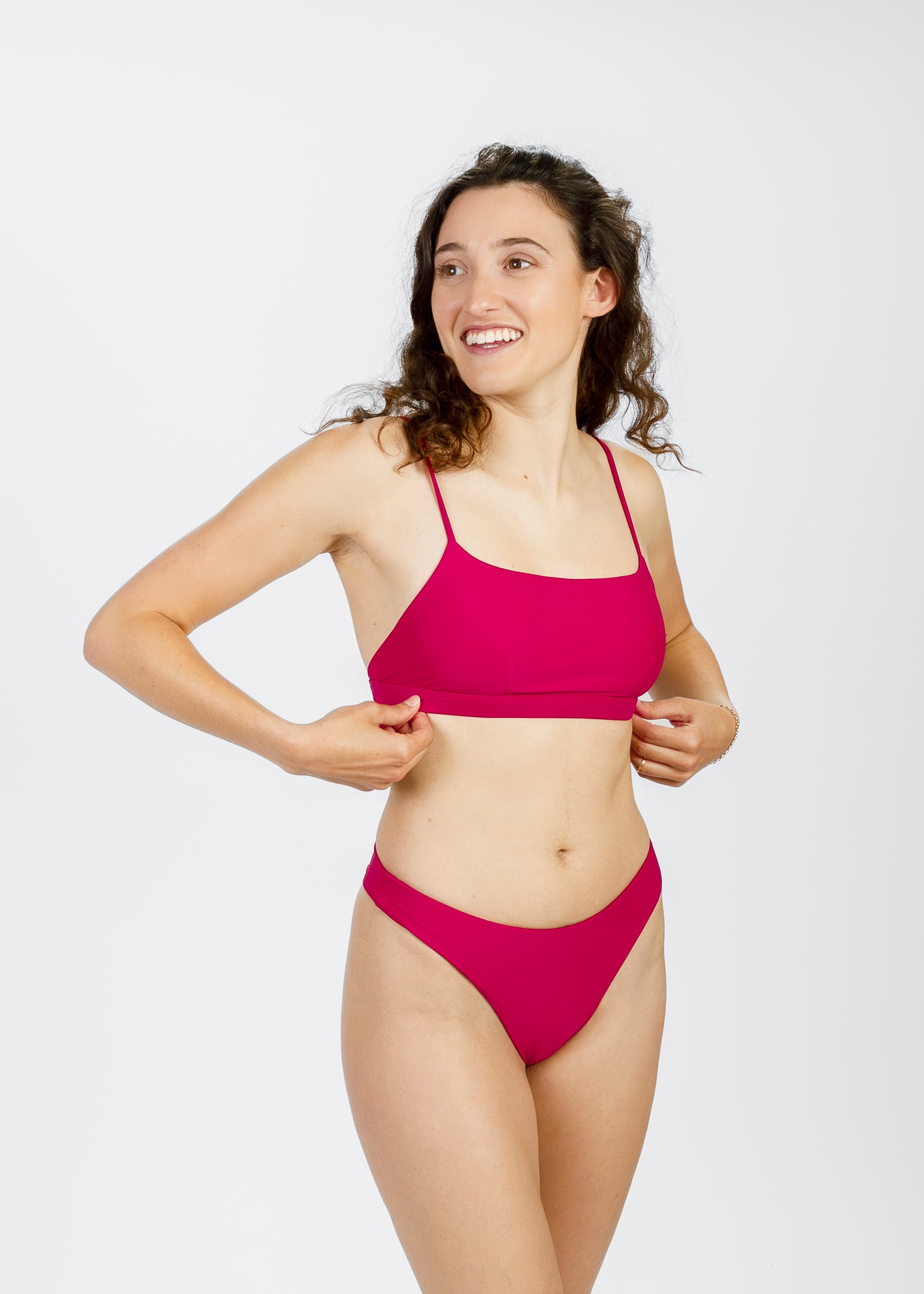 Front view of a smiling woman adjusting her square-neck pink bikini top from Tamara, designed sustainably for stylish support.