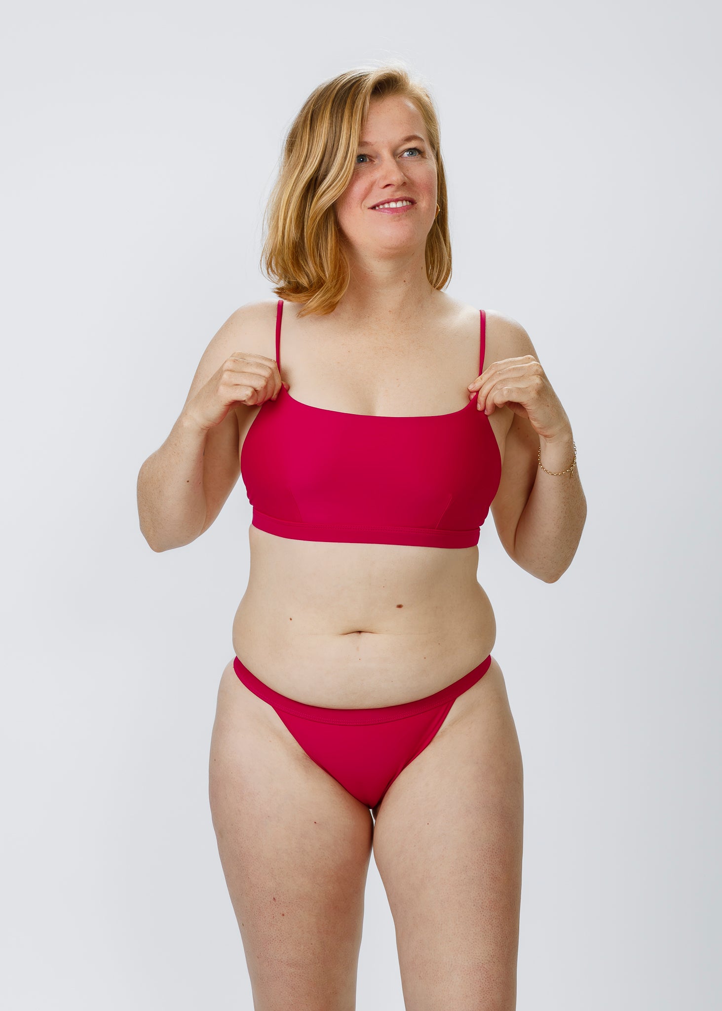 Front-facing view of a woman gently adjusting her sustainable pink bikini top by Tamara, featuring a modern, minimalist square neckline.