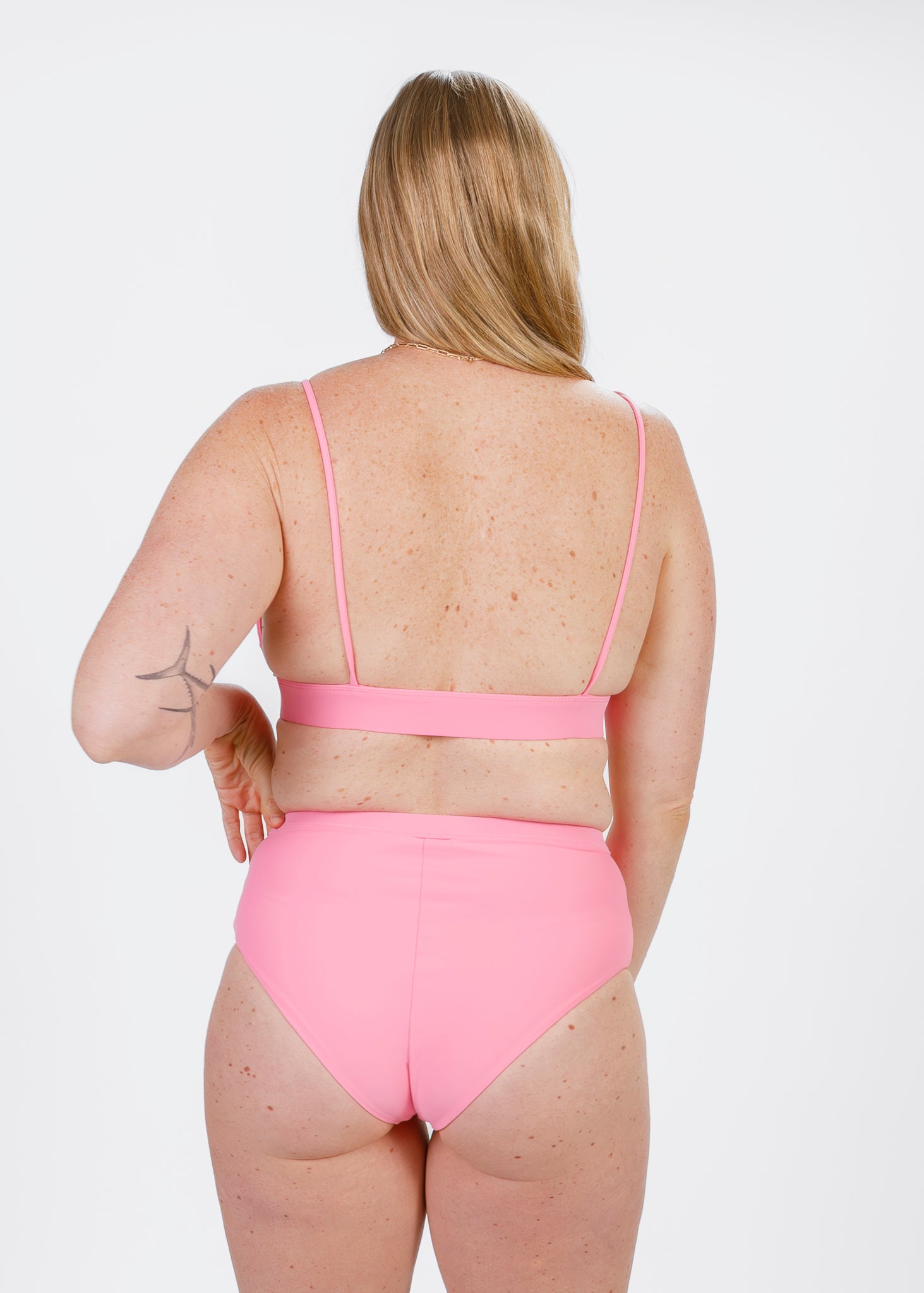 Back view highlighting comfortable coverage of pastel pink high-waisted bikini bottoms on a softly freckled skin tone.