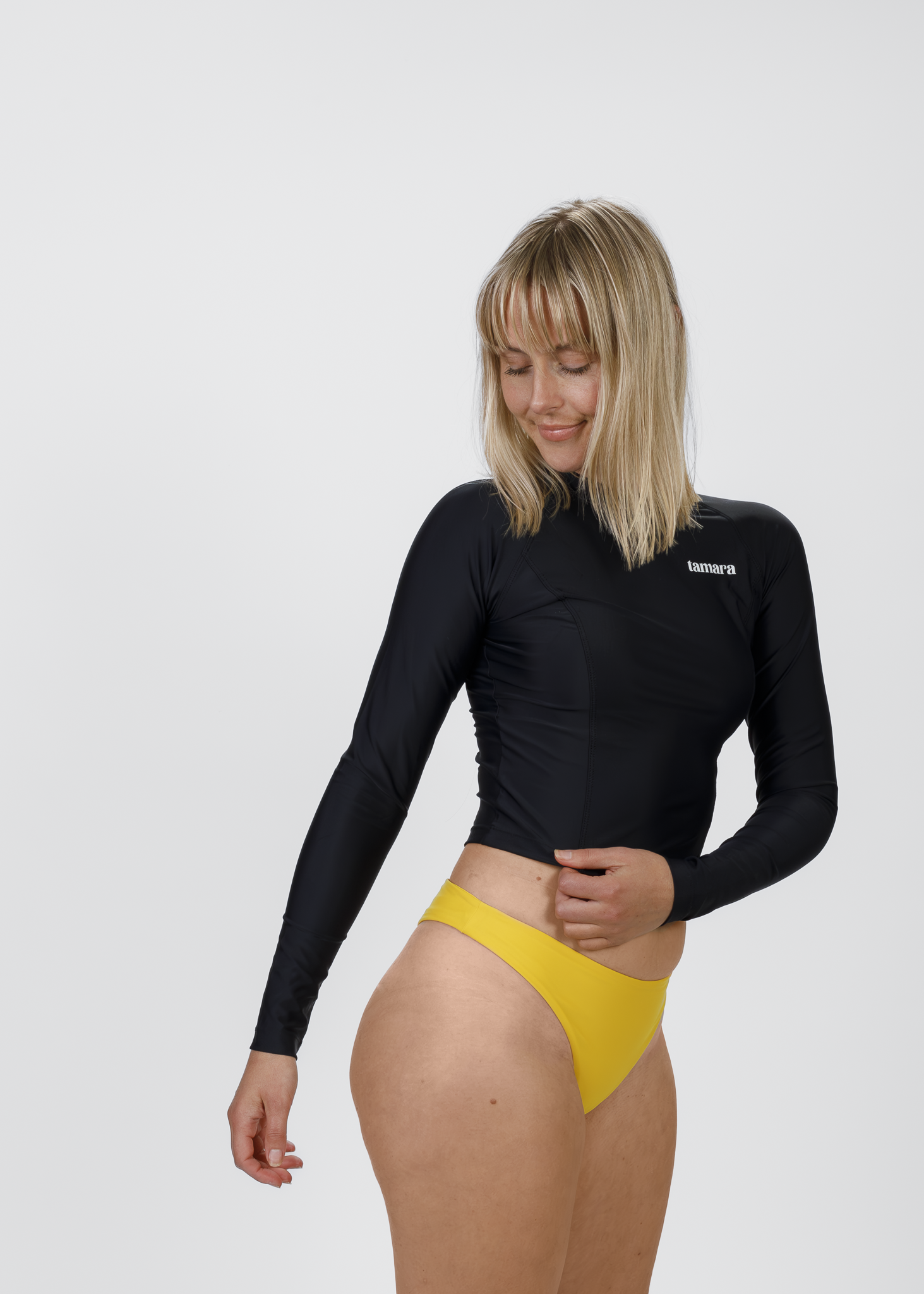 Side view of a model showcasing Tamara’s high-cut yellow bikini bottoms paired with a sleek black rash vest, ideal for surfing and sun protection.